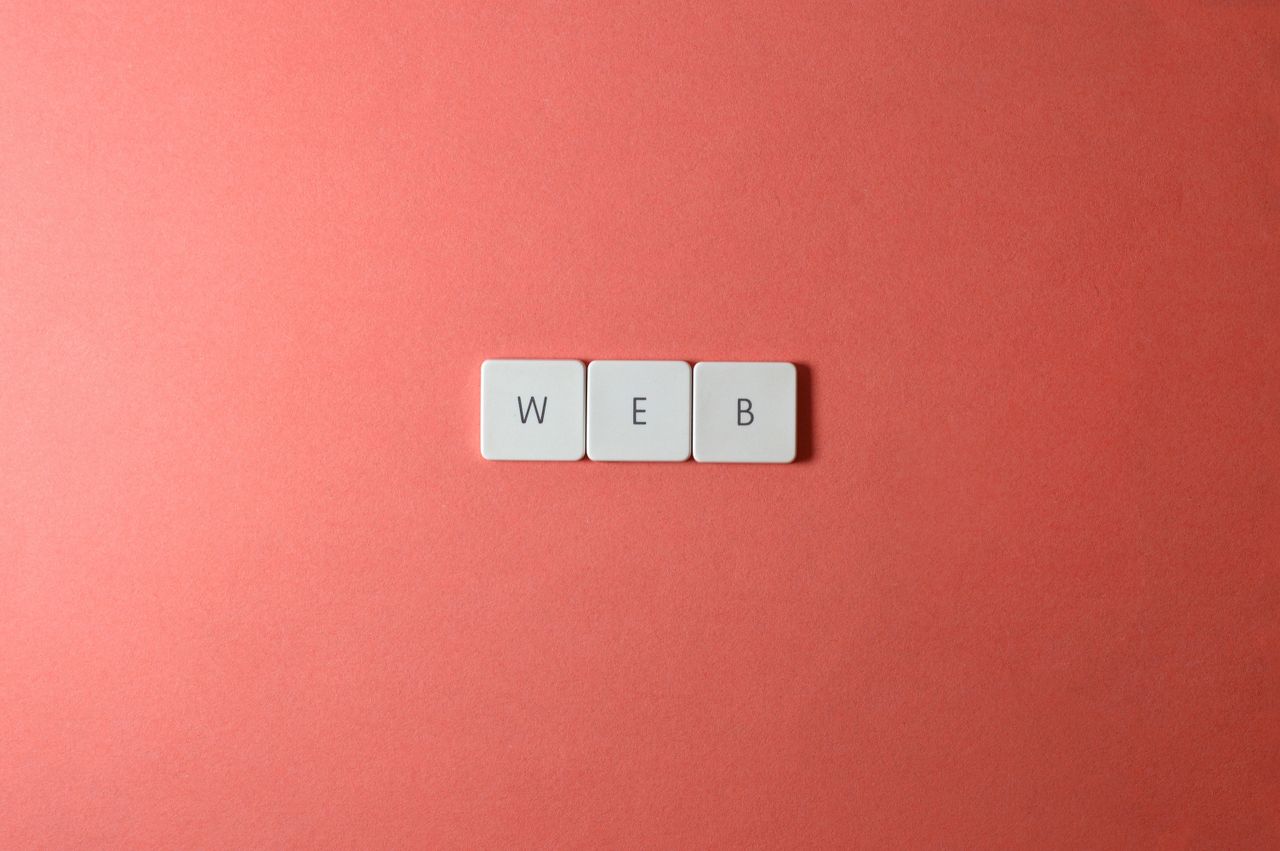 hero-img-01 A minimalist photo featuring the word WEB spelled with keyboard keys on a red background.